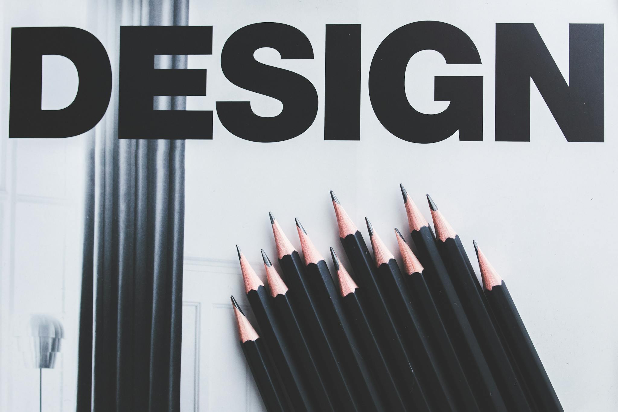 Black pencils arranged creatively next to large typography 'DESIGN'.